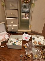 Wooden jewelry box with mirror and drawers, with some jewelry pieces in boxes and on table in front