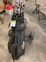 Full view of Callaway black golf bag on wheels with several golf clubs inside and some pockets visible, placed on a cement floor.