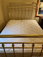 Full view of queen brass bed with mattress and visible bedspread