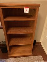 Front view of light oak wooden bookcase with three shelves and no doors, showing wood grain and finish.
