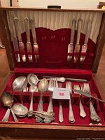 Full view of assorted vintage silverplate flatware pieces inside the red felt-lined wooden storage box.