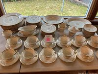 Full view of the Syracuse China Governor Clinton pattern set with multiple plates, bowls, cups, saucers, a gravy boat, sugar bowl, and creamer visible on table near window.