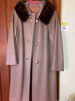 Full view of the camel wool vintage coat with brown fur collar and large buttons, hung on a wooden door
