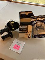 Photo showing the black dual eyepiece View-Master viewer alongside open box containing reels and instruction booklet.