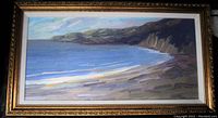 Frontal view of a signed impressionist oil painting of a coastal seascape with cliffs and ocean, in ornate gold frame.