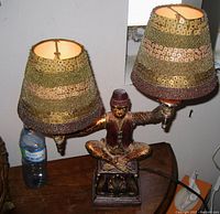 Front view of figural monkey twin-light table lamp on wooden surface showing beaded shades lit.