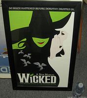 Framed poster showing the green face of Wicked Witch of the West and white face whispering Glinda, flying monkeys flying.
