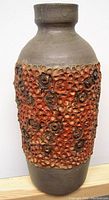 Front angled view of textured pottery vase showing circular indented and raised decorations with mottled brown and orange glazes.