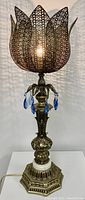 Full view of the gilt metal filigree lamp illuminated to show the detailed petal-shaped metal shade and blue crystal drops around the neck.