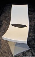 Front view of white molded chair seat with metal base on dark background