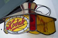 Side perspective of stained glass lamp showing Kodak Film logo in red and yellow on a cream and red glass background, with black wiring attached.