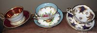 Front angle showing all three teacups with saucers, highlighting the colors and patterns: red/gold, blue floral, and dark blue/gold floral sets.