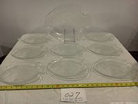 Nine clear fish-shaped glass plates arranged on a white surface, one plate is prominently displayed up front on stand, tape measure shown for scale.