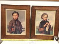 Framed Albert Anker lithographs of boy on left and girl on right, shown with measuring tape to indicate size.