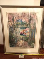 Image of the framed lithograph artwork showing open doors in a garden with children playing inside. The frame is wood painted cream with a white matte border.