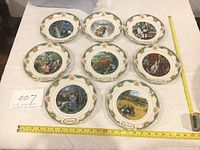 All eight collectible plates arranged in two rows, showing their decorative border and center artwork, with measuring tape showing 8-inch diameter