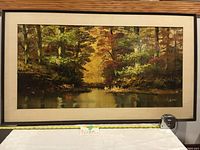 Frontal view of framed large oil painting showing autumn forest landscape with water reflecting trees, with measuring tape showing approximate width.