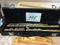 Open black carrying case holding the disassembled silver plated flute and a yellow cleaning cloth laid on the table.