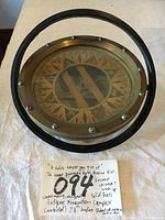 Top view of the solid brass circular compass mounted in a metal frame, showing the patented design note below the compass on paper.