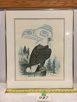 Framed artwork front view showing eagle image with mat and gold frame against a wooden background and measuring tape on bottom edge.