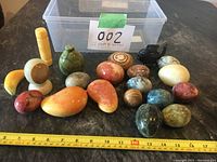 Full overview of 21 polished marble figurines including fruits, eggs, and fish with clear box in background and measuring tape in front