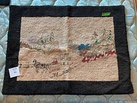 Full view of the hooked rug showing the village scene with black border