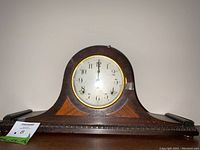 Full side view showing wooden curved mantle clock case with decorative inlay and carved base details. Includes auction tag and handwritten dimensions.