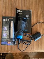 Photo of Braun sealed Ear & Nose Trimmer packaging, Braun Series 5 electric shaver with charger and instruction manual on table.