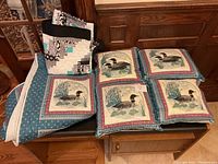 Photo showing folded modern black, white, and turquoise quilt beside the double Canadian Loon quilt and four matching loon-themed pillows on a wooden bench.