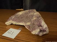 Large amethyst rock with visible purple and white crystalline textures on a wooden surface, showing its size and condition.