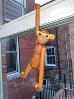 Side view of the teak wood monkey figurine hanging by one arm, showing the finish and craftsmanship on wood surfaces.