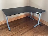 Full view of the black corner desk placed in a corner showing its curved front edge and silver metal legs.