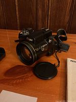 Nikon Coolpix 8800 camera with lens cap on wooden surface next to user manual