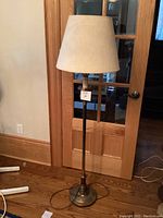 Full view of one brass tone metal standing lamp with beige fabric shade, showing height and overall look.