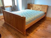 View of pine queen bed frame with mattress shown in bedroom with hardwood floors near window.