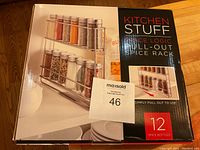 Front view of unopened box showing product image of 2-tier pull-out spice rack with 12 bottles, brand and product name visible.
