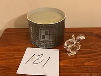 The Swarovski crystal squirrel displayed next to the original round box without its lid, showing the branding and foam insert inside the box.