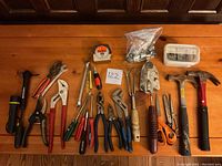 Overview of all tools laid out on wooden surface showing pliers, screwdrivers, hammers, scissors, tape measure, garden tools, and flashlight.