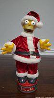 Front view of 12-inch Homer Simpson figurine dressed as Santa Claus with red velvet suit, black belt, and red Santa hat.
