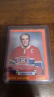Front of 1973-74 Henri Richard hockey card in protective plastic sleeve showing player portrait in Canadiens uniform and relevant text