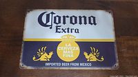 Front view of the Corona Extra metal beer sign showing logo, yellow stripe with emblem and text: 'LA CERVEZA MAS FINA', 'IMPORTED BEER FROM MEXICO'