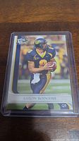 Front side of Aaron Rodgers rookie checklist football card featuring him in uniform with a football.