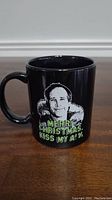 Front view of the black mug showing Clark Griswold's face and green holiday text