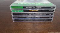 Stack of five PlayStation game cases showing titles: Final Fantasy Tactics, Driver, Who Wants to Be a Millionaire 2nd Edition, NHL Championship 2000, Tiger Woods PGA Tour Golf