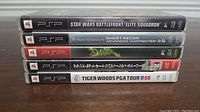 Side view of five Sony PSP game cases showing titles on the spine: Star Wars Battlefront: Elite Squadron, Tom Clancy's Ghost Recon Advanced Warfighter 2, Daxter, Grand Theft Auto: Liberty City Stories, Tiger Woods PGA Tour 08.