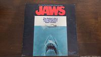 Front sleeve of JAWS soundtrack showing iconic shark emerging towards swimmer with large red JAWS logo and text about the movie.