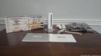 Nintendo Wii console upright on gray stand next to two white Wii controllers with cables, power and video cables coiled, and two instruction manuals.