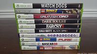 Stack of ten Xbox 360 game cases showing titles on the spines: Watch Dogs, LEGO Batman 2 DC Super Heroes, Split/Second, Dark Souls II, Far Cry 3, Call of Duty Black Ops II, LEGO Batman, PURE, NASCAR 08, LEGO Marvel Super Heroes.
