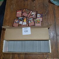 Full cardboard box filled with a large collection of Magic: The Gathering cards, with some cards spread above the box.