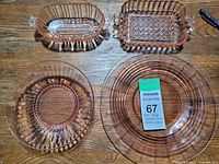 Four pieces of pink Depression glass displayed on a wooden surface: an oval pickle dish, rectangular butter dish, ribbed bowl, and a ribbed glass plate.